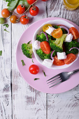 Light salad with broccoli, cherry tomatoes and feta cheese in a white ceramic bowl. Top view