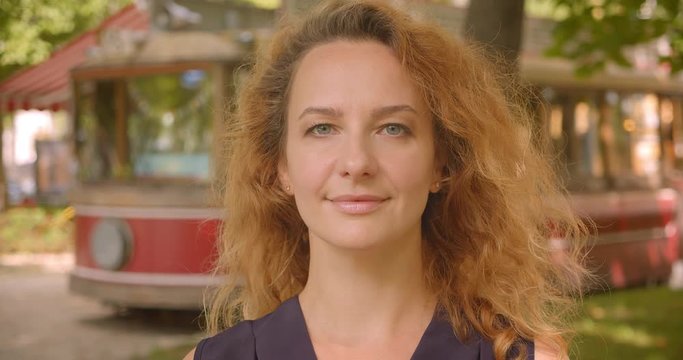 Closeup portrait of adult attractive redhead female looking at camera in park outdoors
