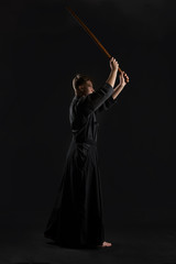 Kendo guru wearing in a traditional japanese kimono is practicing martial art with the shinai bamboo sword against a black studio background.