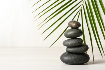 Stack of spa stones and palm leaf on table against white background, space for text