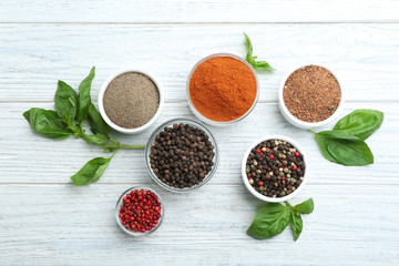 Bowls with different kinds of pepper and leaves on white wooden table, flat lay