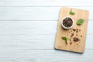 Wooden board with mixed pepper corns and basil leaves on white table, top view. Space for text