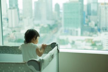 Baby girl is standing in cot and look out of window. Asian baby girl in cot