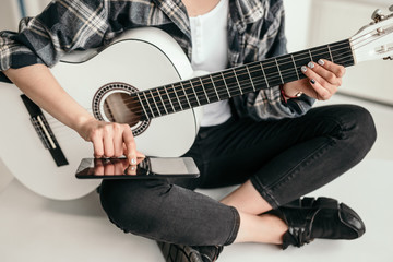 Fototapeta na wymiar Crop woman with smartphone learning to play guitar
