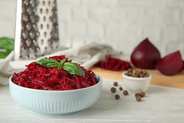 Bowl of grated boiled beets with basil and allspice on white wooden table