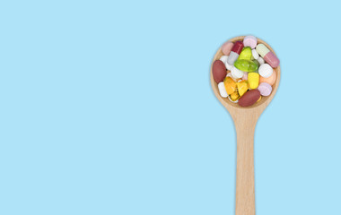 Top view of assorted pharmaceutical medicine pills, tablets and capsules in wooden spoon isolated on blue background, Dietary supplement healthcare product, Copy space.