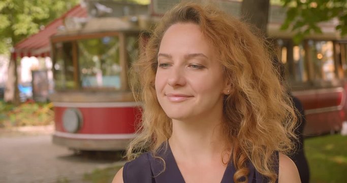 Closeup portrait of adult pretty redhead female looking at camera smiling cheerfully in park outdoors