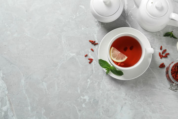 Obraz na płótnie Canvas Cup of healthy goji tea with lemon on grey table, flat lay. Space for text