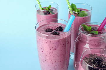 Delicious blackberry smoothie in different glassware on light blue background