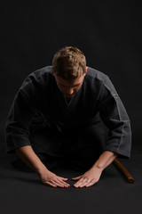 Kendo guru wearing in a traditional japanese kimono is practicing martial art with the shinai bamboo sword against a black studio background.