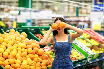 Young girl holds oranges in her hands on the background of shelves with fruits. Model posing in the mall
