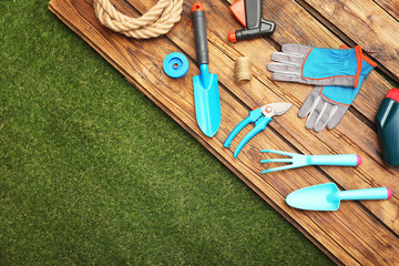 Wooden surface with gardening tools on green grass, flat lay. Space for text
