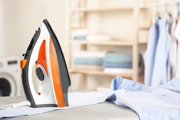 Modern electric iron and clean shirt on board in laundry room. Space for text