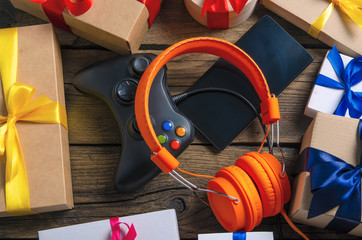 Orange headphones music audio, gamepad, smartphone, mobile phone, box with ribbon bow gift on wooden background, top view