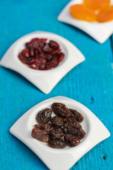 Dried raisins in small white saucers on a wooden blue background.