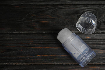 Natural crystal alum deodorant and cap on black wooden table, above view. Space for text