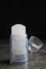 Natural crystal alum deodorant and cap on grey table against black background