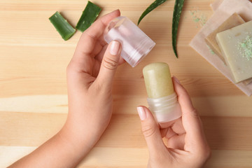 Young woman holding natural crystal alum deodorant at wooden table, top view