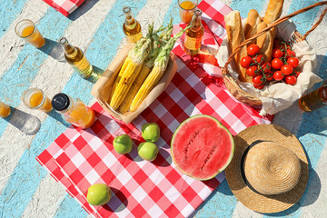 Naklejka na ściany i meble Straw hat and different products for summer picnic on checkered blanket, flat lay