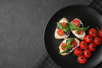 Plate of delicious tomato bruschettas on black background, top view. Space for text