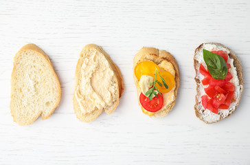 Delicious tomato bruschettas on white wooden background, flat lay