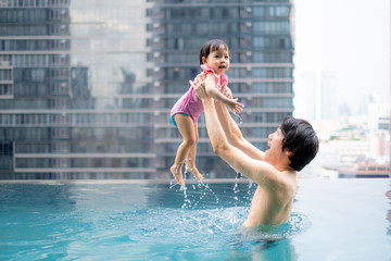 Happy Father rising up baby girl in swimming pool.infants swimming. Asian Baby swimming concept.