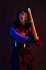Close up shot, Kendo fighter wearing in an armor, traditional kimono, helmet practicing martial art with shinai bamboo sword, black background.