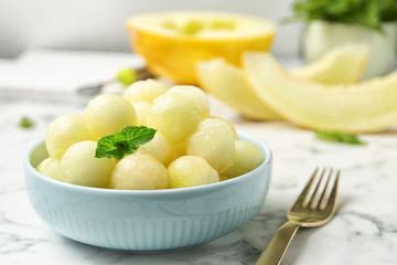 Plate of melon balls with mint on white marble table, closeup