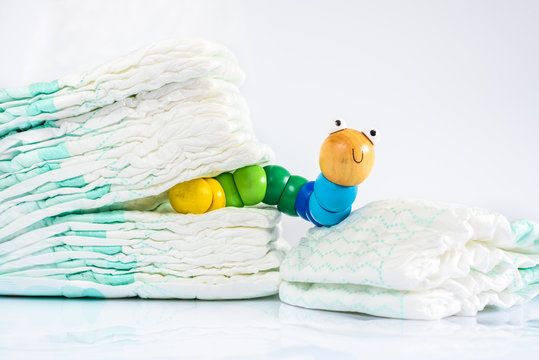 Toy worm with smile next to a pile of diapers, to illustrate concepts of health and childhood intestinal diseases. Isolated on white