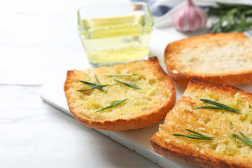 Slices of toasted bread with garlic and herb on white wooden table, closeup