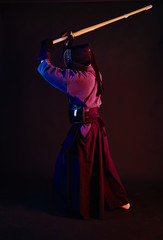 Close up shot, Kendo fighter wearing in an armor, traditional kimono, helmet practicing martial art with shinai bamboo sword, black background.