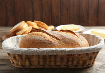 Loaf of tasty fresh bread in wicker basket on wooden table