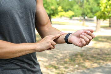 Young man checking pulse after training outdoors, closeup