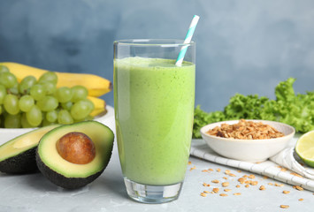 Glass of tasty smoothie and avocado on light grey marble table
