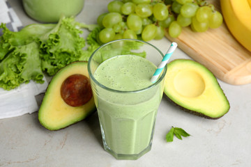 Glass of tasty smoothie and avocado on light grey table