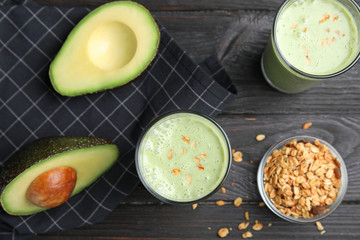 Glasses of tasty smoothie with avocado and oatmeal on black wooden table, flat lay