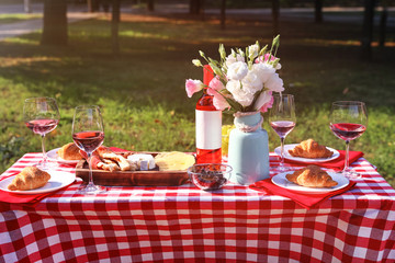Wine, food and flowers on picnic table in park on sunny day