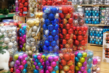 Packaged Christmas balls for decoration prepared for sale in supermarket. Variety of purple, golden, red, green, blue glass balls on shelves of large shop.