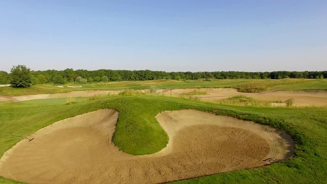 4K aerial footage of golf course. Cinematic top view shot with green grass, ponds, watercourses, palm trees, patches, holes, flags. Drone flies along the field during sunset. Vacation video concept