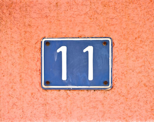 Number 11 / eleven, blue plate on pale pink wall surface.