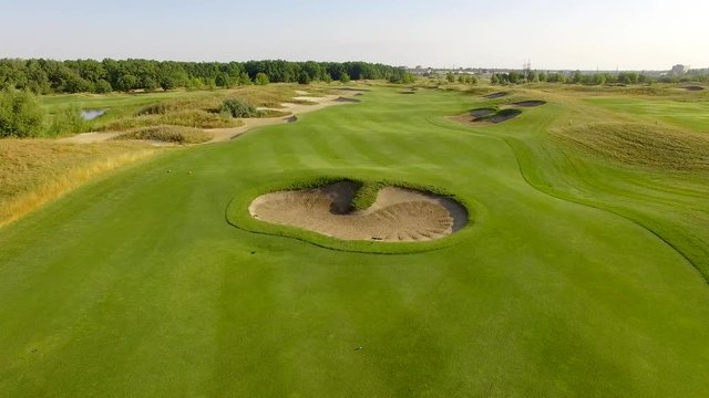 4K aerial footage of golf course. Cinematic top view shot with green grass, ponds, watercourses, palm trees, patches, holes, flags. Drone flies along the field during sunset. Vacation video concept