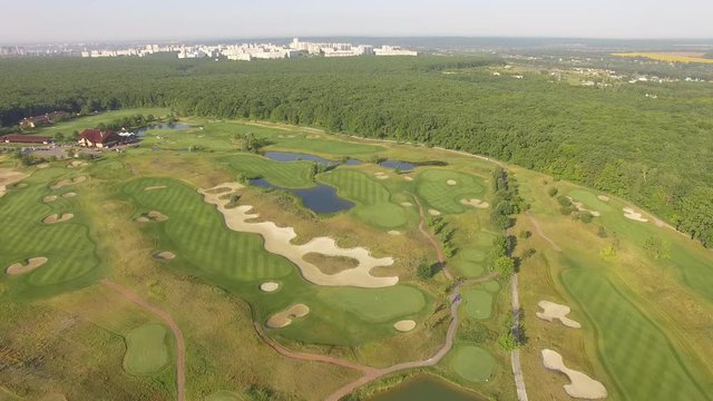 4K aerial footage of golf course. Cinematic top view shot with green grass, ponds, watercourses, palm trees, patches, holes, flags. Drone flies along the field during sunset. Vacation video concept
