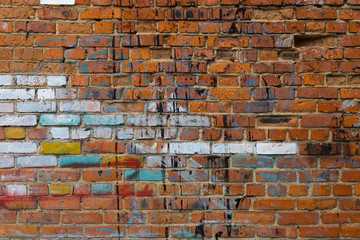 Old red brick wall with colorful spots of paint. Grunge texture.