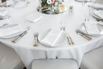 Wedding table setting decorated with fresh flowers. White plates, silverware, white tablecloth and white room. Wedding floristry. Banquet table for guests. Bouquet with roses, hydrangea and eustoma