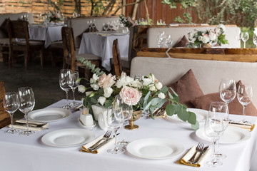 Wedding table setting decorated with fresh flowers in a brass vase. Wedding floristry. Banquet table for guests outdoors with a view of green nature. Bouquet with roses, eustoma and eucalyptus leaves