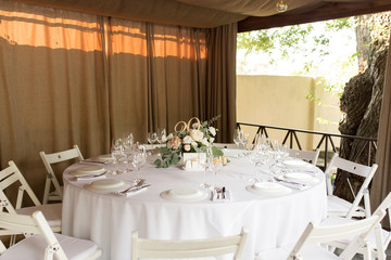 Wedding table setting decorated with fresh flowers in a brass vase. Wedding floristry. Banquet table for guests outdoors with a view of green nature. Bouquet with roses, eustoma and eucalyptus leaves