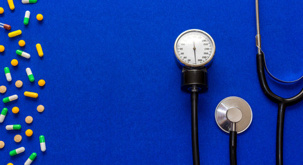 Medical pills, tonometer and stethoscope on the blue surface. Blood pressure measurement. Color...