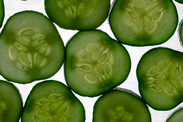 Beautiful, green, glowing cucumber slices lying on a white background. Slices of cucumber, educated flash.