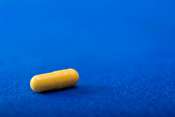 One yellow medical pill. Color capsule medication. Blue background. Health care concept. Free space for text. Medicines. Chemical industry.