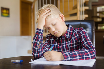 Sad schoolboy writing to notebook at home. Homework. Education, childhood and people concept